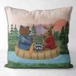 A pillow featuring hand painted art of Bear, moose and raccoon riding down the river in a canoe.