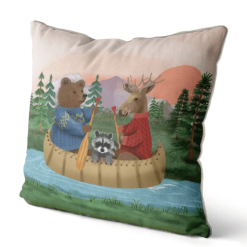 A pillow featuring hand painted art of Bear, moose and raccoon riding down the river in a canoe.
