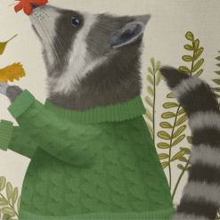 A pillow that displays a raccoon in a green sweater playing in fall leaves closeup view.